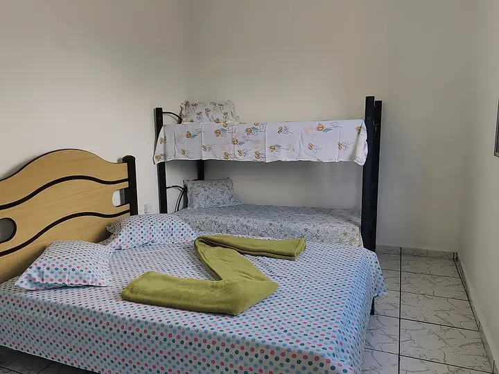 Quarto com cama de casal, beliche e toalhas dobradas sobre a cama